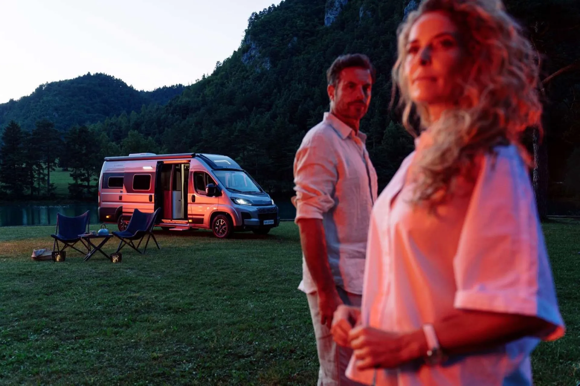 Couple devant un véhicule Neo-NOMAD premium au crépuscule, au bord d'un lac en Provence